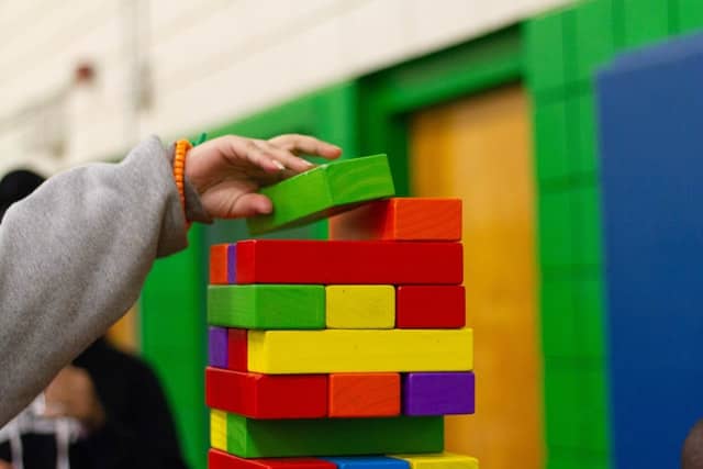 childs hand placing a large colored block on a stack of oversized colored jenga blocks